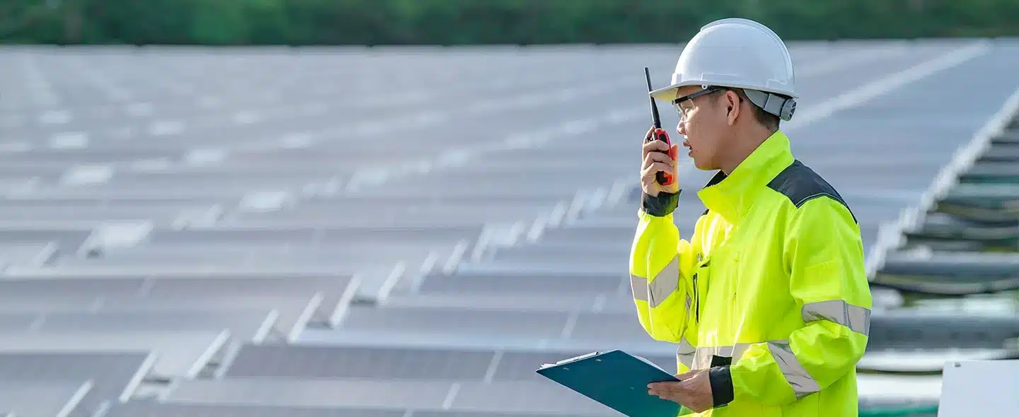 Engenheiro asiático trabalhando ao lado de painéis solares fazendo o monitoramento de usinas solares